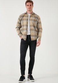 Geel en zwart geruit overhemd over een wit T-shirt, gecombineerd met zwarte skinny jeans en zwarte sneakers met witte zolen.