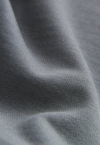 Siva tkanina z drobnim rebrastim vzorcem. Tkanina je rahlo zmečkana, kar poudarja subtilne odtenke in svetlobo.