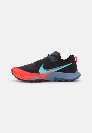 Black athletic shoe with bright red toe, blue sole, turquoise Nike swoosh, and black laces on a light gray background.