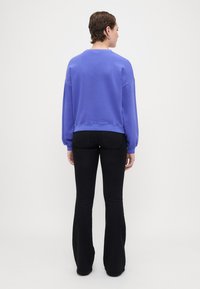 Sudadera púrpura con cuello redondo, hombros caídos y mangas largas, combinada con vaqueros negros acampanados. Textura suave, diseño casual.