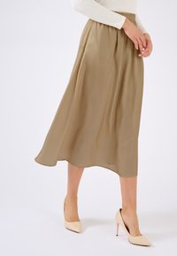 Beige midi-rok van lichtgewicht stof met een elastische tailleband, gecombineerd met naakte puntige hoge hakken. De rok heeft een vloeiend ontwerp.