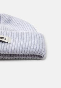 Gorro de malha azul claro com textura canelada, dobra na bainha e um pequeno rótulo branco com texto preto de um lado.