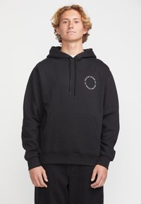 Hoodie noir en tissu doux et texturé avec une poche avant et un capuchon avec cordon de serrage. Présente un logo circulaire sur le côté gauche de la poitrine.