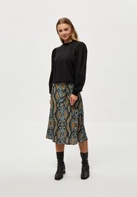 Crni dugovedri top s nabranim ramenima, kombiniran s midi suknjom s uzorkom zmije u plavoj i smeđoj boji. Crne gležnjače upotpunjuju izgled.