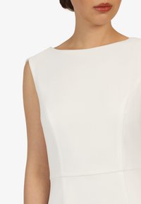 Weißes ärmelloses Kleid mit einem Bootsausschnitt und tailliertem Oberteil. Glatte Textur mit minimalen Nähdetails an der Taille.