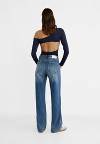 Navy long-sleeve top with an open back, paired with faded blue wide-leg jeans. The jeans feature a back patch and classic five-pocket design.