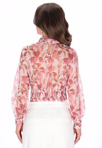 Transparante, bloemenblouse in roze en crèmekleuren met een smocktail, lange pofmouwen en een knoopsluiting op de rug.
