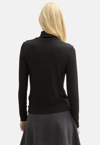 Schwarzes Langarmoberteil aus geripptem Stoff mit hohem Kragen, kombiniert mit einem grauen, schwingenden Rock. Die Rückansicht zeigt eine glatte Textur und ein einfaches Design.