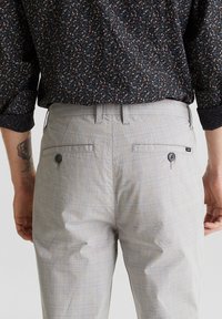 Vaaleanharmaat ruudulliset housut, joissa on kaksi takataskua, nappikiinnitys ja vyölenkit, yhdistettynä tummaan kukkakuviolliseen paitaan.