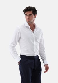 Camicia bianca a maniche lunghe con un sottile motivo a quadri, colletto classico e chiusura a bottoni. Abbinata a pantaloni blu scuro in tessuto liscio.
