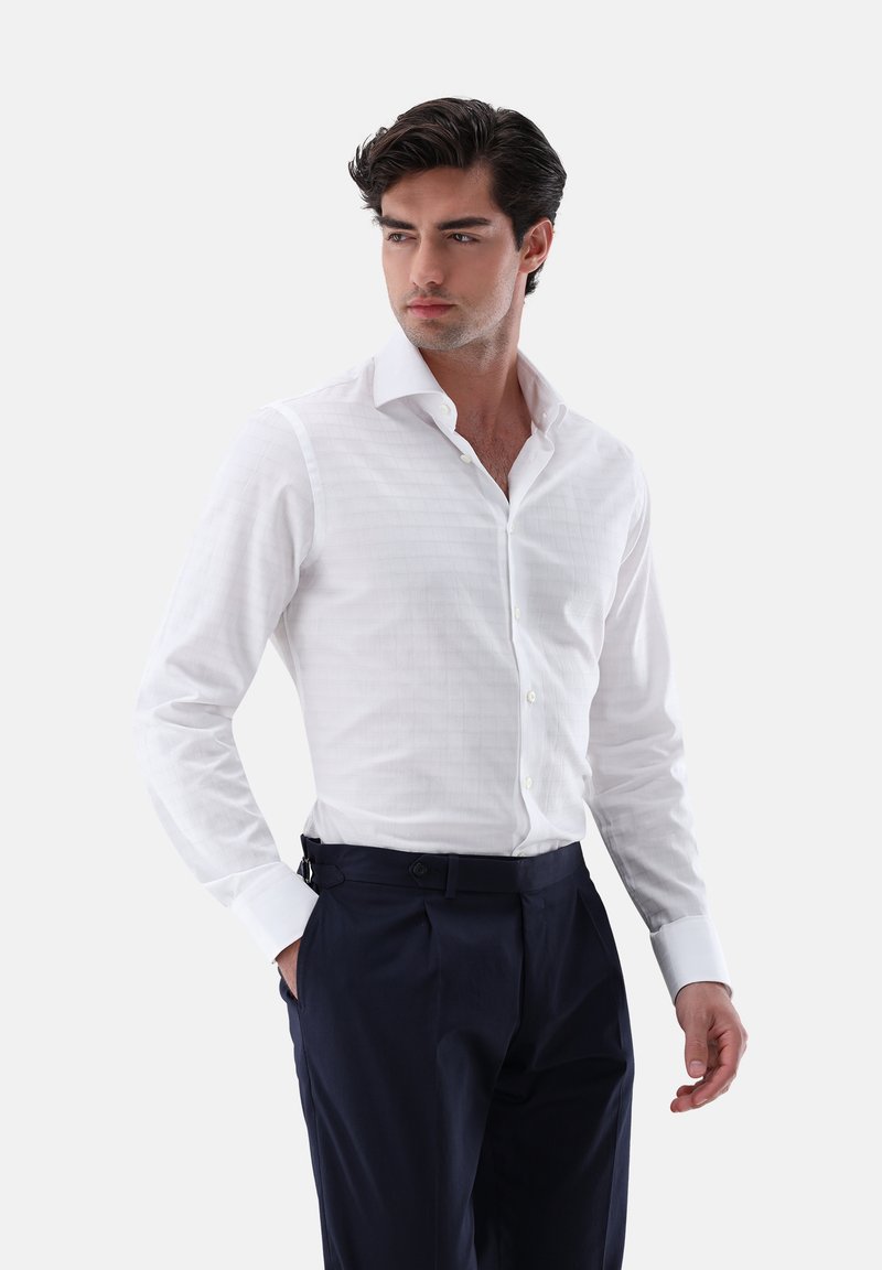 Camicia bianca a maniche lunghe con un sottile motivo a quadri, colletto classico e chiusura a bottoni. Abbinata a pantaloni blu scuro in tessuto liscio.