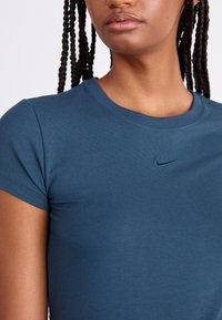 Tirkīza krāsas īsām piedurknēm T-krekls, izgatavots no mīkstas kokvilnas, ar smalki izšūtu Nike logo uz krūtīm. Gluda tekstūra un pielāgota forma.