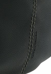 Dettaglio di una borsa in pelle nera con superficie testurizzata, caratterizzata da cuciture grigie lungo una cucitura e un sottile logo del marchio in rilievo.