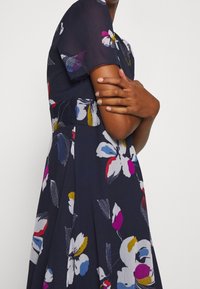 Blumenkleid aus navy Stoff mit kurzen Ärmeln. Verfügt über farbenfrohe Blumenmuster in Pink, Weiß und Gelb. A-Linien-Silhouette und strukturierte Oberfläche.