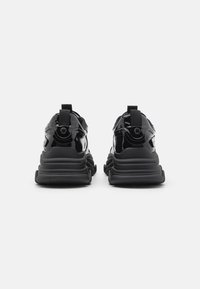 Svarte patentlær sneakers med en teksturert svart såle, som har fremtredende bakre snorene og slanke, polstrede detaljer.