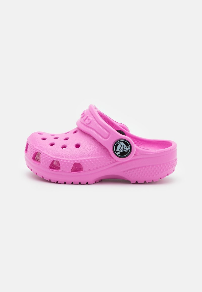 Sabot rose à enfiler avec des trous de ventilation et une bride réglable au talon avec un logo circulaire sur fond blanc.