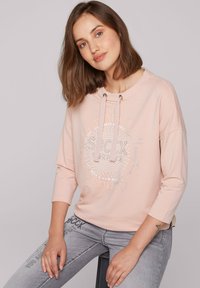 Felpa leggera rosa con collo rotondo, cordino, maniche a tre quarti e stampa grafica argentata che presenta testo circolare e pois.