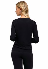 Czarny sweter z długim rękawem o okrągłym dekolcie, o prążkowanej fakturze i dopasowanym kroju. Noszony z czarnymi legginsami, tworzącymi gładką sylwetkę.