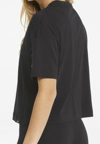 Black cotton t-shirt with short sleeves and a cropped design. Features a round neckline and subtle stitching details along the hem.