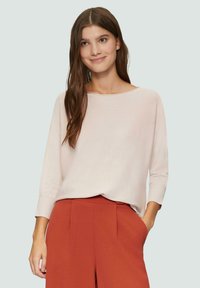 Helles rosa Langarmshirt mit weitem Ausschnitt und gerippten Bündchen, kombiniert mit rostfarbenen, hochtaillierten Hosen. Glatte Stoffstruktur.