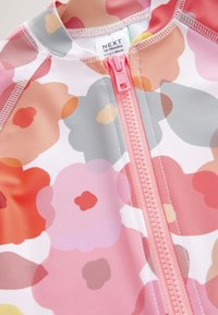 Badeanzug mit Blumenmuster, das mehrfarbige Blüten in Pink-, Rot- und Grautönen zeigt. Reißverschluss in Pink; glatter, elastischer Stoff.