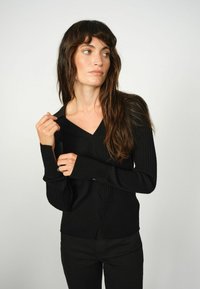 Schwarze, gerippte Strickjacke mit V-Ausschnitt und langen Ärmeln. Mit einer Knopfschließe und weichem, strukturiertem Stoff.