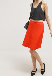 Un débardeur noir ajusté, une jupe rouge évasée et des ballerines noires. La jupe présente une couleur unie et une texture lisse.