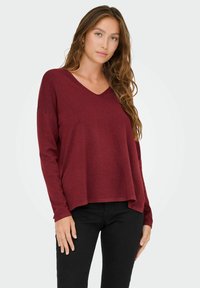 Pullover borgogna a maniche lunghe con scollatura a V, vestibilità comoda e polsini a costine. Realizzato in un tessuto morbido, presenta una finitura testurizzata.