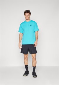 T-shirt Nike turquoise à manches courtes, associé à un short noir. Logo noir notable sur la poitrine et texture de tissu lisse.