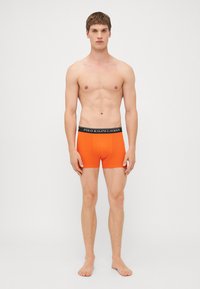 Oranžne bokserice s črnim elastičnim pasom, na katerem je napis "POLO RALPH LAUREN". Gladek material, dolžina do sredine stegen, prilagojen dizajn.