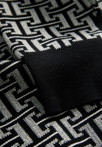 Textil tricotat alb-negru, cu un model geometric repetitiv și o manșetă neagră ribbată solidă. Textură fină și design detaliat.