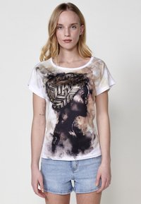T-shirt blanc à manches courtes avec un design en silhouette noire représentant un foulard à motifs sur fond aquarelle beige et marron.