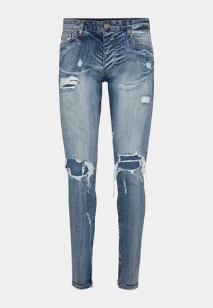 Vaqueros ajustados de mezclilla en azul medio con desgastes y bordes deshilachados. Presenta un cierre frontal con botón y cremallera.