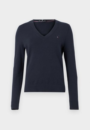 Pull bleu marine à manches longues avec un design en V, en tissu tricoté, avec des poignets côtelés et un petit logo en haut à gauche.