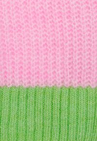 Nahaufnahme von weichem, pinkfarbenem, flauschigem Strickstoff über fest geripptem grünem Strickstoff.