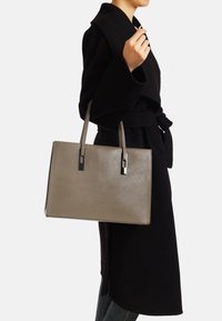 Borsa a tote in pelle beige con forma rettangolare elegante, due manici dritti e accenti in metallo a contrasto. Texture liscia.