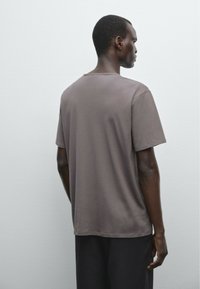 Hnědé bavlněné tričko s volným střihem, krátkým rukávem a kulatým výstřihem, se hladkou texturou a minimalistickým designem.