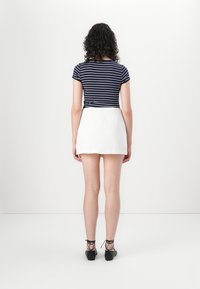 Marineblå og hvite striper kortermet topp kombinert med en hvit miniskjørt og svarte snøredde sko, sett fra baksiden. Glatte teksturer.