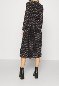 Zwart lange mouwen jurk met een geplooide rok, voorzien van een delicate gepatterneerde ontwerp in roze, en gecombineerd met zwarte enkelhoge laarzen met hak.