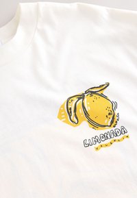T-shirt blanc avec un graphisme de citron jaune aux contours noirs et le texte « LIMONADA VALENCIA » en bas. Texture douce en coton.