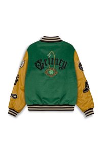 Chaqueta de terciopelo verde con mangas de cuero amarillo, detalles bordados en negro y cuello de canalé a rayas. Presenta parches en las mangas.