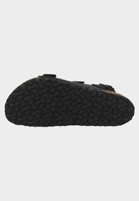 Suola di scarpa nera con un pattern ondulato, caratterizzata da una superficie testurizzata per una presa migliore. I bordi sono arrotondati e il materiale appare gommoso e resistente.
