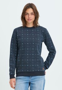 Sweatshirt marine avec un motif géométrique bleu clair, col rond et poignets côtelés. Associé à un jean en denim bleu clair.