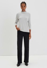 Pull en maille côtelée gris clair avec des manches longues et un col haut, associé à un pantalon droit noir, avec des coutures subtiles et des poches latérales.