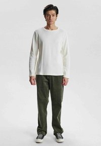 Weißes langärmliges, geripptes Strickoberteil, kombiniert mit olivgrünen Cordhosen und schwarzen Turnschuhen. Schlichtes Design mit rundem Halsausschnitt.