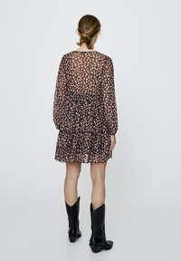 Robe noire à motifs floraux avec manches longues, taille froncée et tissu transparent. Portée avec des bottes de cowboy noires à bouts pointus et coutures décoratives.