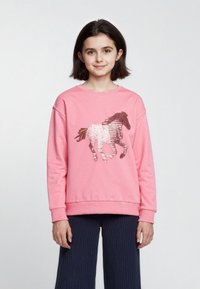 Felpa rosa con un design di un cavallo in paillettes. Il tessuto è morbido, con un collo rotondo e polsini a coste, abbinata a pantaloni larghi blu navy.