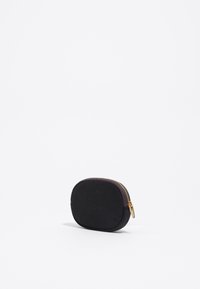 Bolso blando negro con forma redondeada, tejido texturizado, cremallera dorada y un acento morado oscuro que contrasta en la cremallera.