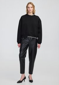 Czarna bluza z oversize'owym krojem i prążkowanym dołem, z metalowymi detalami w kolorze srebra przy dekolcie. Połączona z czarnymi skórzanymi spodniami.