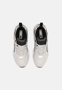 Světlé šedé sportovní boty s síťovinou a syntetickými překryvy, černé akcenty, texturované podrážky a podpisové logo na jazyku a boku.